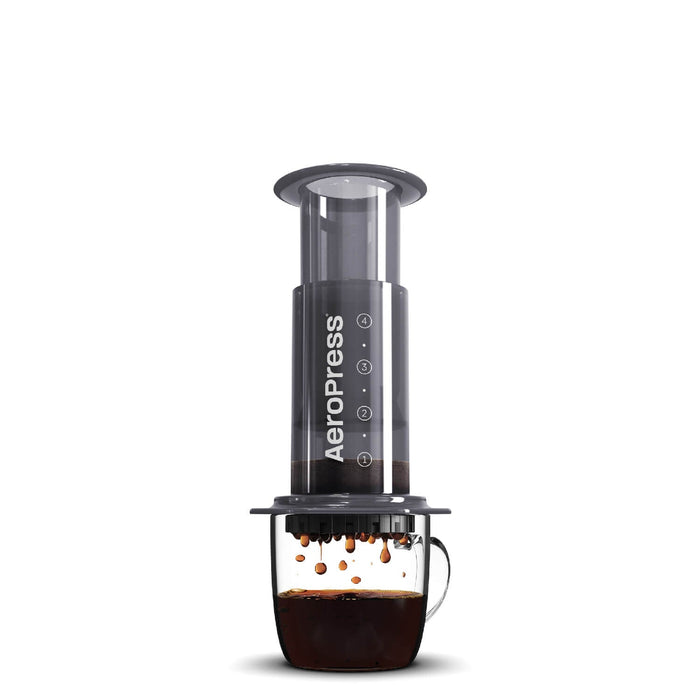Cylindrical coffee press device with a clear chamber and black body, positioned over a glass mug containing brewed coffee.